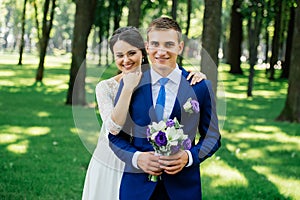 Yong beautiful smiling bride and groom hugs in the park. Bride embraces the groom. Couple in love at wedding day