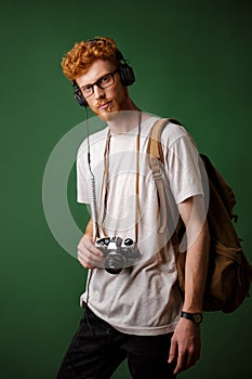 Yong readhead bearded hipster with backpack holding retro camera