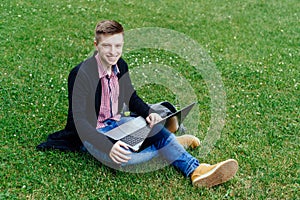 Yong smiling man  in plaid shirt and jacket sitting on green law.