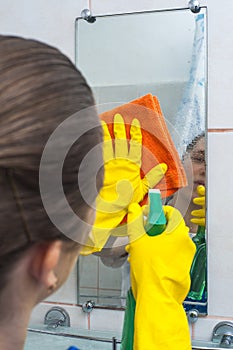 Yong woman cleaning the mirror with rag and spray
