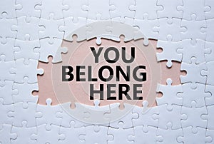 You belong here symbol. White puzzle with words You belong here. Beautiful pink background. Business and You belong here concept. photo