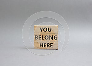 You belong here symbol. Wooden blocks with words You belong here. Beautiful grey background. Business and You belong here setbacks