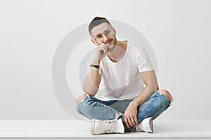 You are so boring. Studio shot of attractive caucasian unshaven guy in glasses, sitting with crossed legs on floor