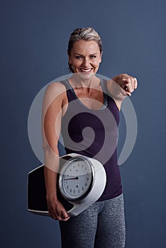 You can do it too. Studio portrait of an attractive mature woman holding a weightscale and pointing at the camera