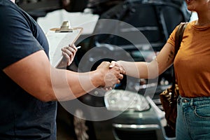 You can trust us to deliver on time. a woman shaking hands with a mechanic in an auto repair shop.