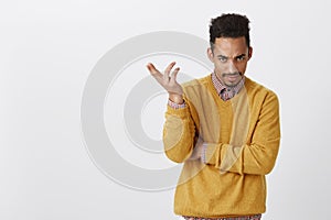 Are you dumb. Portrait of annoyed good-looking male with afro haircut in yellow clothes, gesturing, expressing confusion