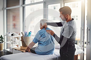 Are you feeling any discomfort over here. a young male physiotherapist assisting a senior patient in recovery.