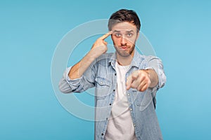 You are idiot! Portrait of man in shirt showing stupid gesture and pointing to camera, blaming for insane plan