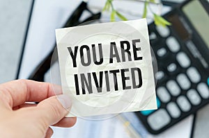 You Are Invited text card in hand with blurred bokeh lights in the background