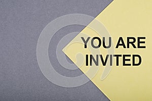 YOU ARE INVITED text on a yellow paper with gray