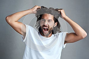 You make me want to pull my hair out. Studio shot of a young man screaming against a grey background.