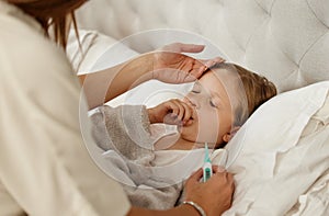 You might have a fever. Shot of a woman taking her little girls temperature with a thermometer in bed at home.