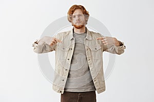 You need me. Cool and confident attractive redhead artistic guy in beige jacket over striped t-shirt pointing at himself