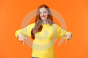 You need see this, check it out. Cheerful gorgeous redhead girl in yellow sweater, smiling and pointing down, recommend