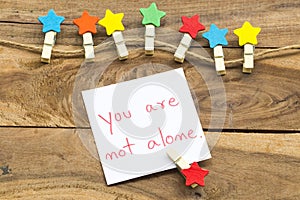 You are not alone message card handwriting with colorful wooden star clips arrangement flat lay postcard style