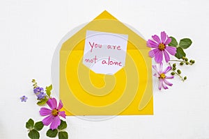 You are not alone message card handwriting in yellow envelope with pink  flowers cosmos arrangement flat lay postcard