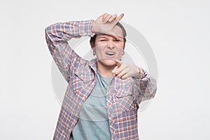 You are outsider. Annoyed good looking woman, tilting head and showing loser sign over forehead