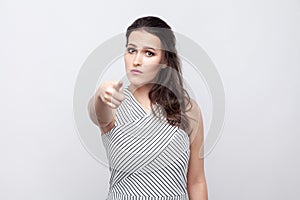 You. Portrait of serious beautiful young brunette woman with makeup and striped dress standing, looking and pointing at camera