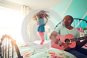 You rock, dad. a cheerful little girl jumping on her bed at home while her father plays the guitar.