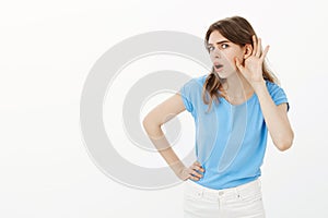 You say what. Portrait of intrigued interested cute woman in blue t-shirt, bending towards camera, holding hand near ear