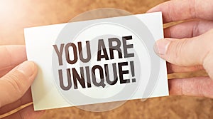 YOU ARE UNIQUE word inscription on white card paper sheet in hands of a businessman. recap concept. red and white paper