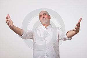 You are welcome concept. Cheerful mature man in white shirt gesturing welcome sign and smiling