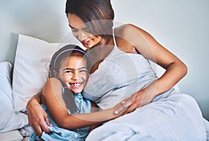 You will always be my firstborn. Portrait of a cheerful little girl relaxing on the bed with her pregnant mother at home