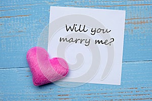 YOU WILL MARRY ME? word on paper note with pink heart shape decoration on blue wooden table background. Love, Wedding, Romantic