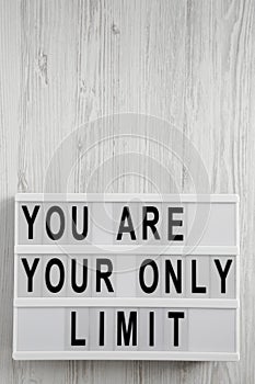 `You are your only limit` words on a lightbox over white wooden background, top view. Overhead, from above. Flat lay. Copy space