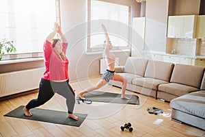 Youbng plus size model and well-built woman doing exercise together. Stretching up and standing in yoga pose. Asana