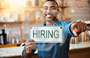 Youd make a great addition to our business. Portrait of a young man pointing while holding up a hiring sign in his store