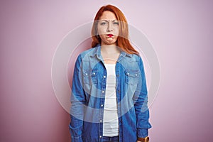 Youg beautiful redhead woman wearing denim shirt standing over isolated pink background puffing cheeks with funny face