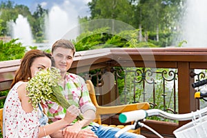 Youg female smelling flowers while sitting on a bench with a boy