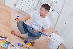 Youg painter sitting on floor holding paintroller