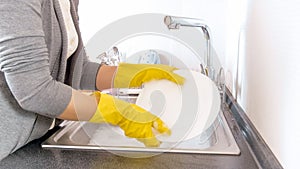 Yougn housewife in rubber gloves washing dishes in sink on kitchen