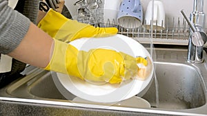 Yougn woman in yellow rubber gloves washing dishes on kitchen