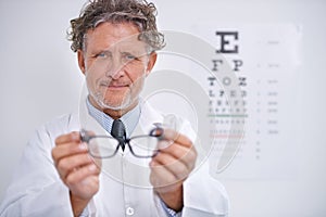 Youll see the world more clearly with these. Portrait of a mature optometrist holding a pair of glasses.