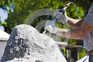 YounaYoung man at work with compressed air chisel and protective gloves to carving a stone block man at work with hammer and