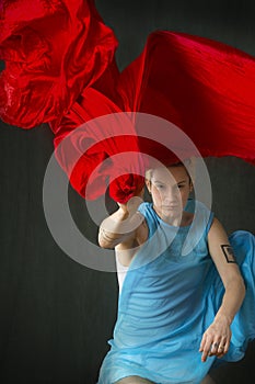 Yound woman in blue cape throwing a red scarf.