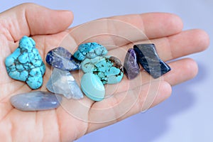 Yound woman is holding a collection of various raw mineral gemstones in her palm