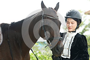 Young 20s Asian woman in horse riding suit with beautiful animal outdoors. Female ride tall smart