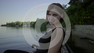 Young 30s woman in black dress sitting on bench on the riverside at the sunset. Lady enjoying her time alone by the