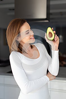 Young 30s woman showing avocado at kitchen