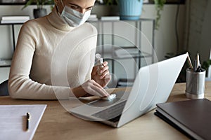 Young 30s woman wearing facial mask sanitizing keyboard.