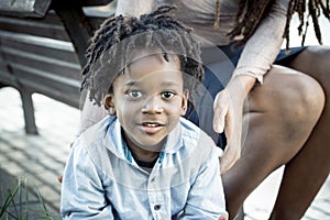 Young 5 yo boy smiling at the camera. Portrait close up of little guy enjoying time outdor with his mommy. Family with black