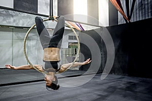 Young acrobatic woman hanging on aerial hoop