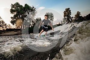 Young active brunet man riding on the wakeboard near the lakeside