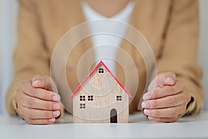 Young active business woman hands in casual dress sitting and protecting house model on white table. Property insurance and