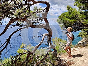 Young active feamle tourist wearing small backpack walking on coastal path among pine trees looking for remote cove to photo