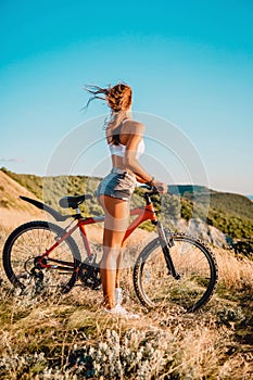 Young active girl with mountain bicycle in white shirt, shorts and white sneakers outdoor
